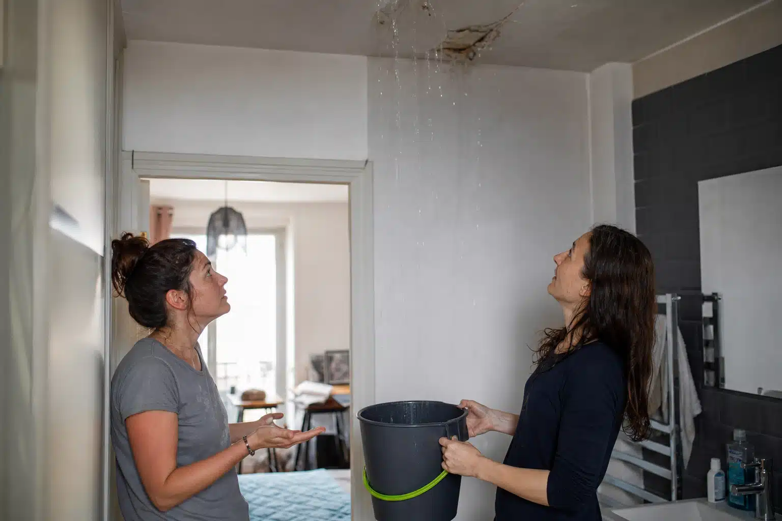 Deux femmes tenant un seau sous une fuite au plafond